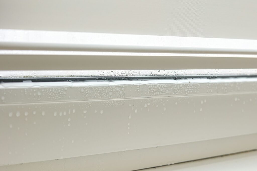 Water droplets condensation on white metal-plastic frame of window indoors room. High humidity. Mois