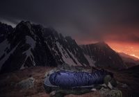 Der Schlafsack. Tourist in Schlafsacklager im Hochgebirge. Nachtfotografie im Freien mit schöner Landschaft.