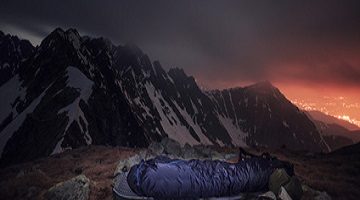 Der Schlafsack. Tourist in Schlafsacklager im Hochgebirge. Nachtfotografie im Freien mit schöner Landschaft.