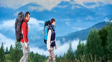 Wanderwege In den Bergen wandern. Der Kerl und das Mädchen mit Rucksäcken sind auf dem Weg auf einem Hügel mit einer schönen Landschaft von Bergen im Dunst. Konzept des aktiven wandernden Lebensstils im Freien.
