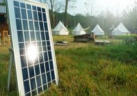 Solartechnik fürs Campen. Sonnenkollektoren oder Solarzellen und im Hintergrund Zelte.