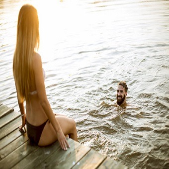 Baden im See. Junges Paar an einem See, während Frau auf Pier sitzt und Mann im See schwimmt.