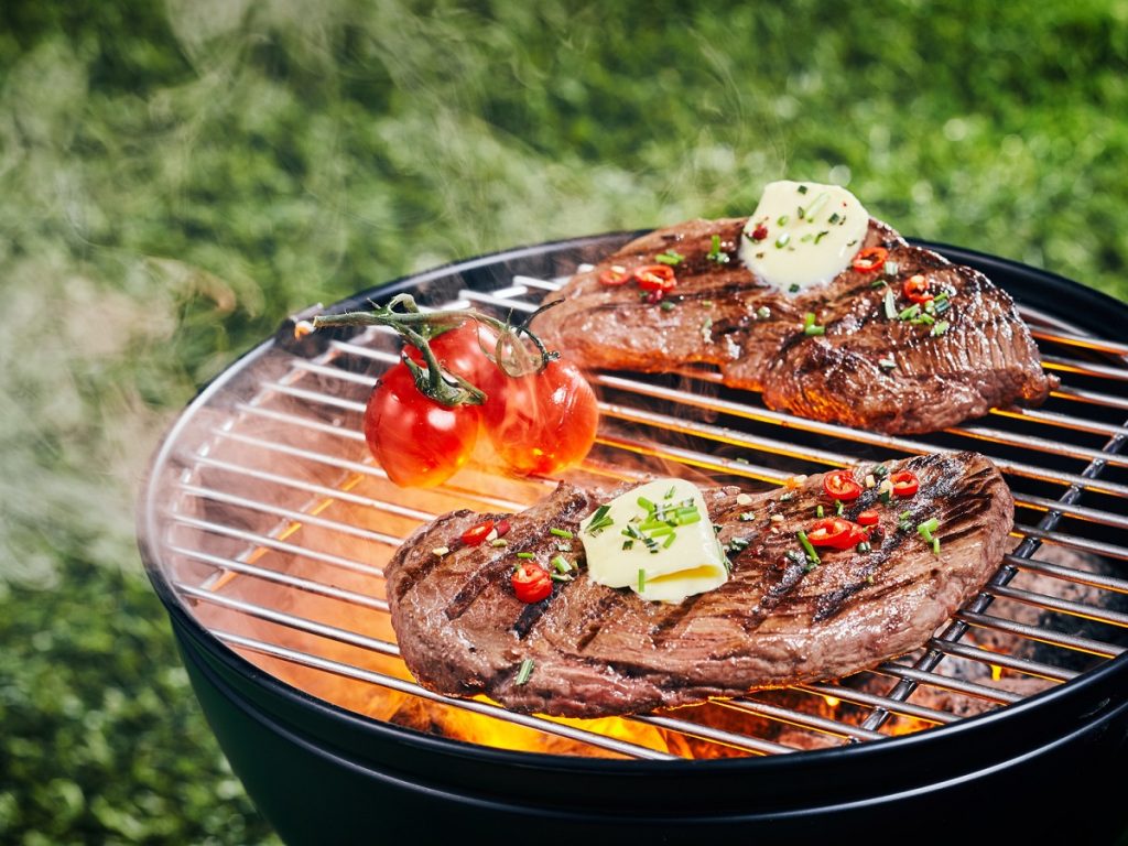 Canpingküche. Zwei zarte Portionen Rumpsteak, gegrillt auf einem Grillfeuer bei einem Picknick oder Campingplatz, garniert mit Kräutern, Gewürzen und einem Stück Butter.