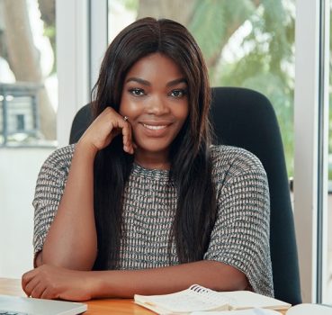Charming stylish African American woman sitting at table in office smiling at camera