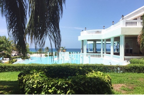 A large white house with a pool and lots of greenery.