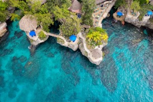 Aerial view of thatched-roof structures on a rocky coastline with crystal-clear blue waters in Ocho Rios, Jamaica.
