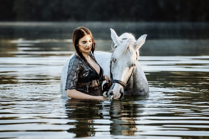 Eine junge Frau geht mit ihrem Pferd im See schwimmen