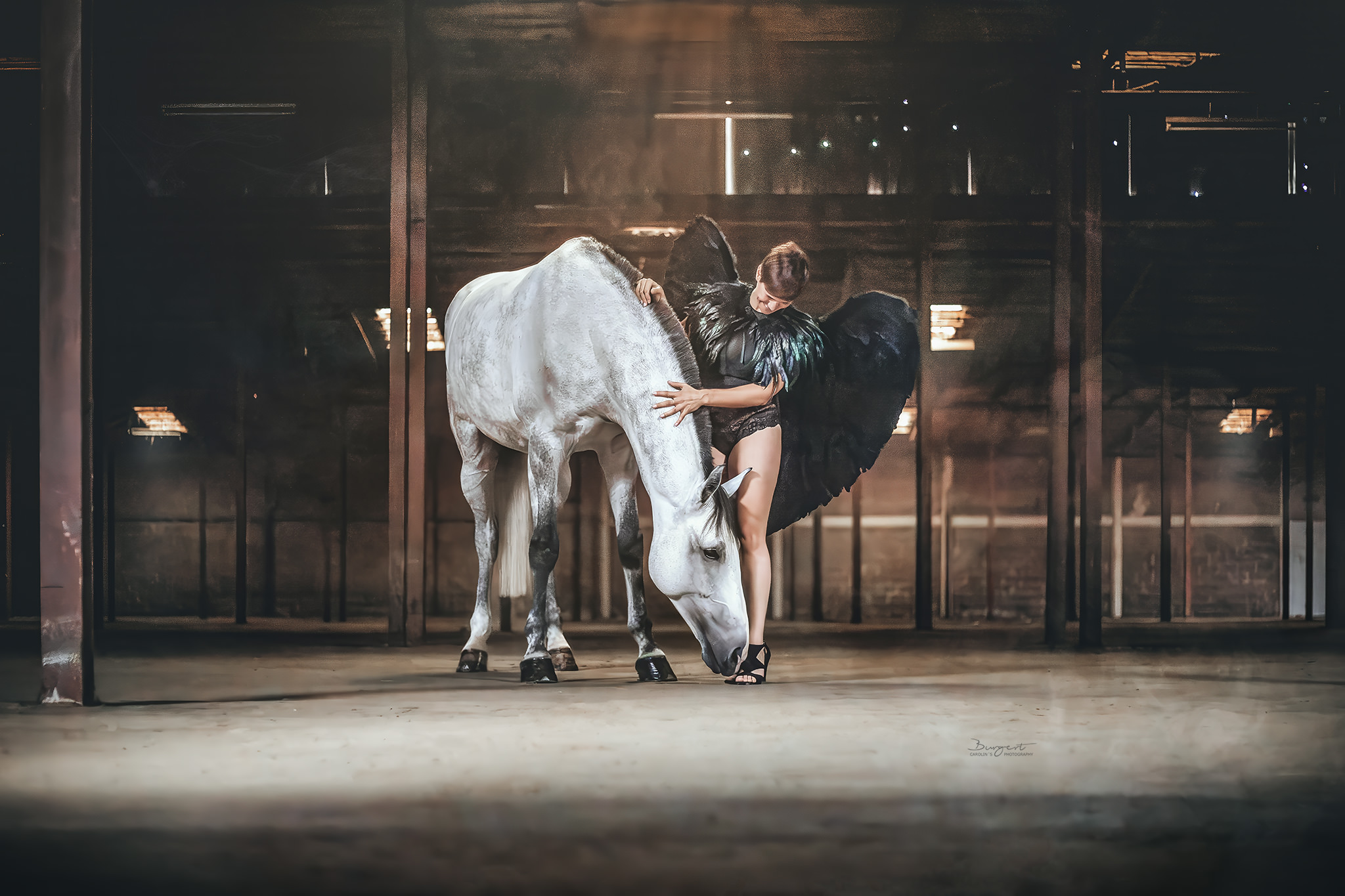 Frau mit schwarzen Flügeln und weißem Pferd in Industriehalle