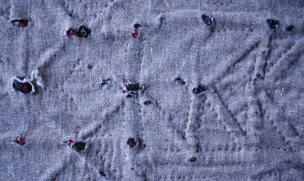Grey fabric backing worn through into holes where bulky joins in the top fabric have caused wear.