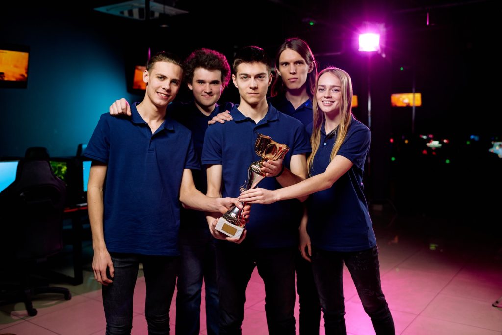 Five cheerful and successful e-sports competition winners holding golden statue