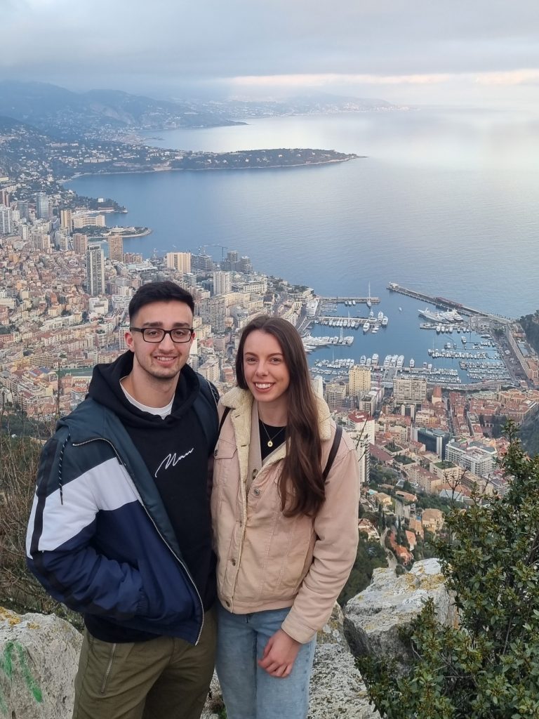 Charlotte and Haydn stood at the top of a mountain with the view of Monaco below