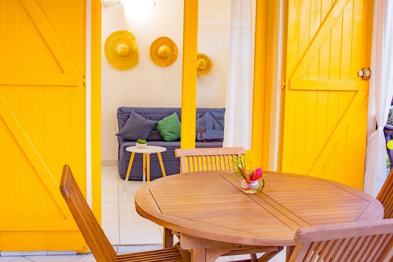 Terrasse aux portes jaunes avec table ronde donnant sur la salle de séjour