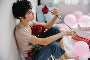 Frau, traurig, mit einer roten Rose und Luftballons sitzt auf dem Boden