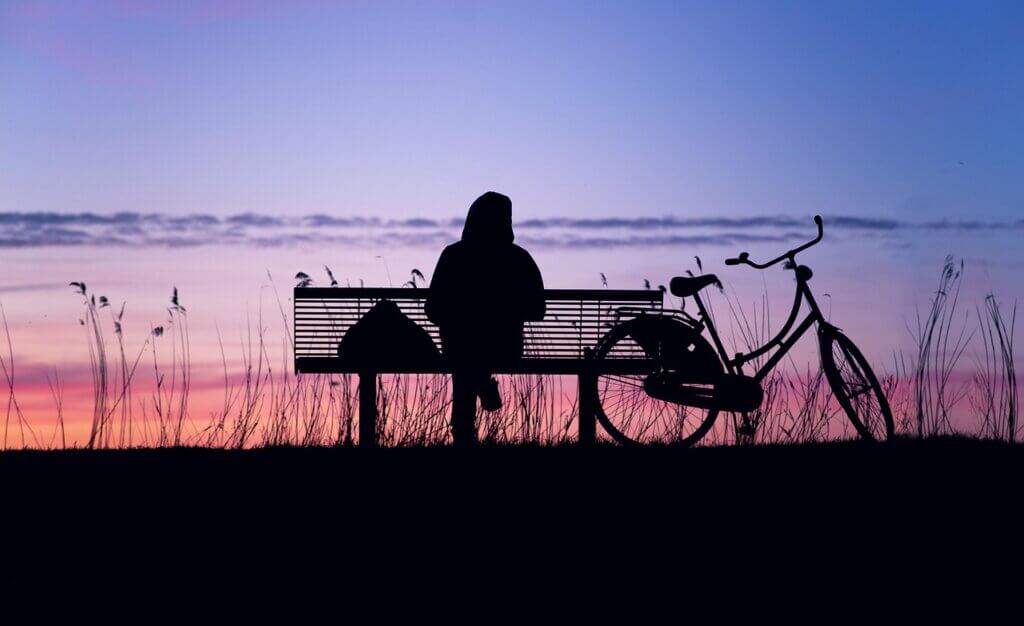 Sonnenuntergang und eine Person sitzt auf der Bank