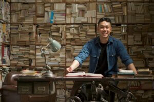 In diesem Blogartikel findest du alles um die UWE-Studie zum Wohlgefühl bei Jugendlichen. Auf dem Bild ist zu sehen: Ein lächelnder Mann vor vielen Büchern.