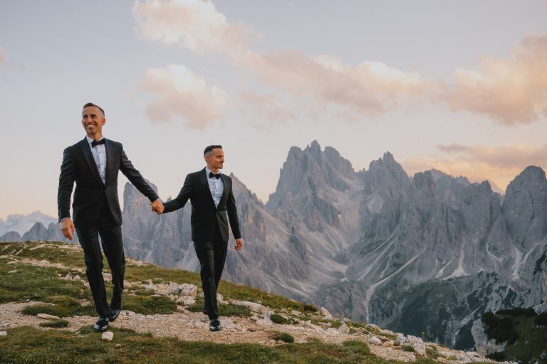 Two grooms holding hands on a mountaintop during elopement in the Dolomites, photo by Christin Eide Photography