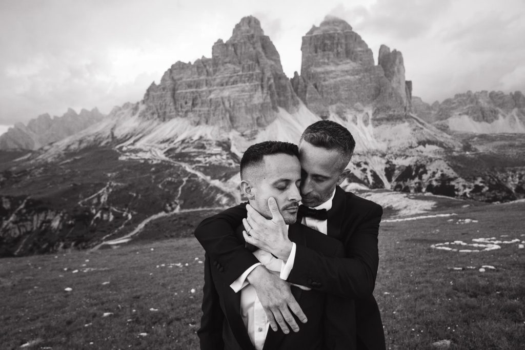 Two grooms embracing on a mountaintop during elopement in the Dolomites, photo by Christin Eide Photography