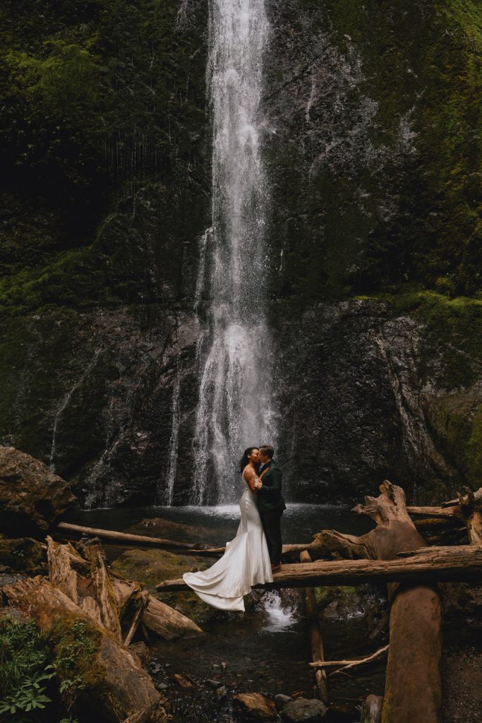 Brides kissing in front of waterfall during their adventure elopement in the Pacific Northwest - photographed by Christin Eide Photography