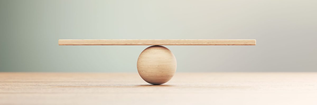 Wooden seesaw scale sitting on wood surface in front of defocused background. Balance concept.