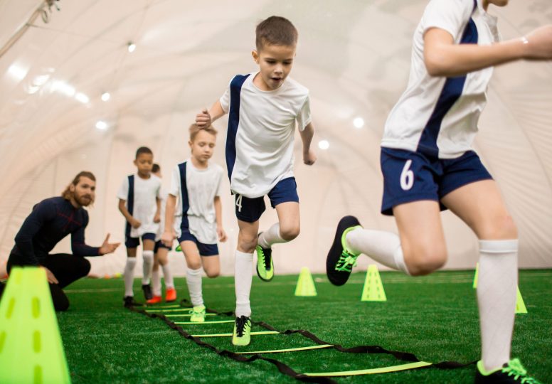 Row of boys running on green football field during training with instructor