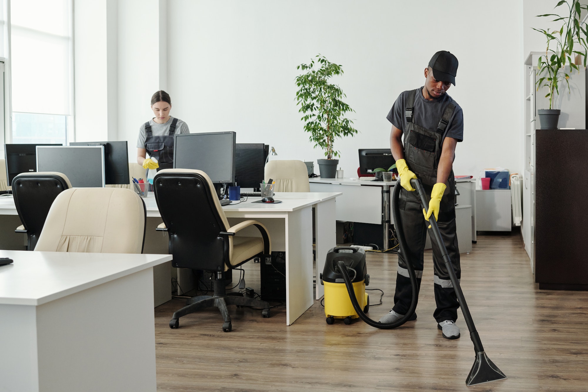 Young African American man in workwear cleaning floor of contemporary office