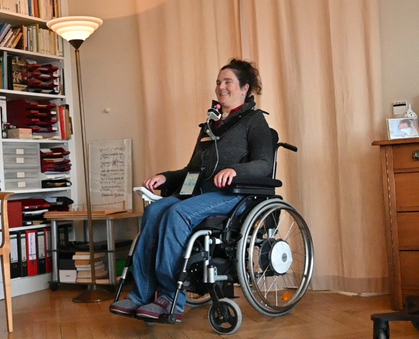 Eine Frau sitzt in ihrem Zimmer in einem Rollstuhl und lacht