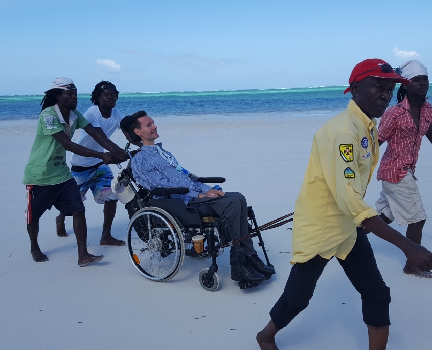 Oliver Jünke wird mit seinem Rollstuhl am Strand durch den Sand gezogen