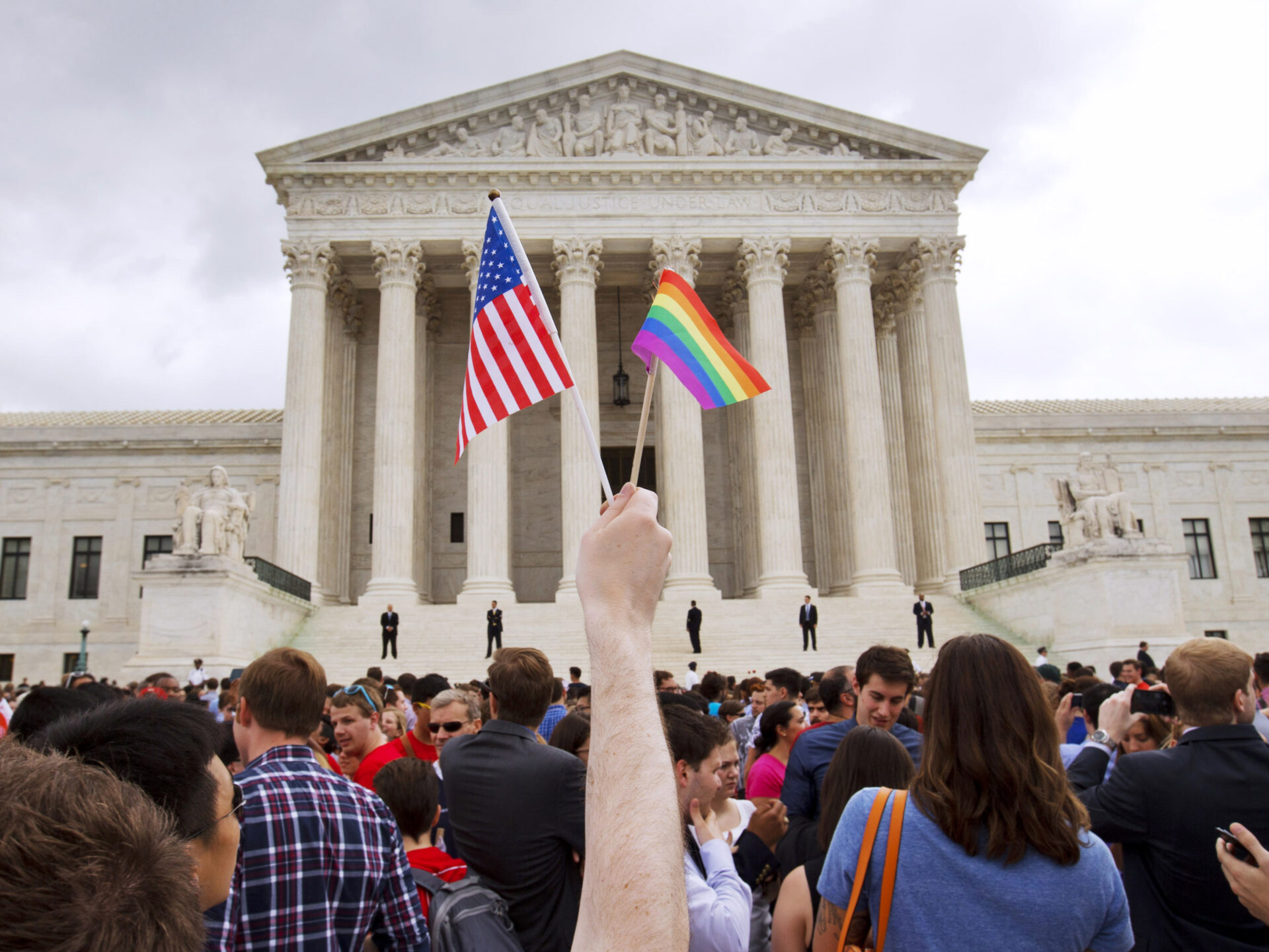 Homem com bandeira lgbt e bandeira americana em frente ao supremo tribunal americano depois de se legalizar casamento entre o mesmo sexo