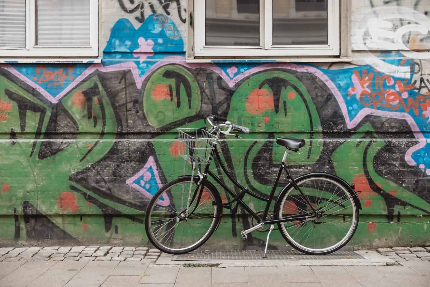 Black bicycle in front of green grafitti art