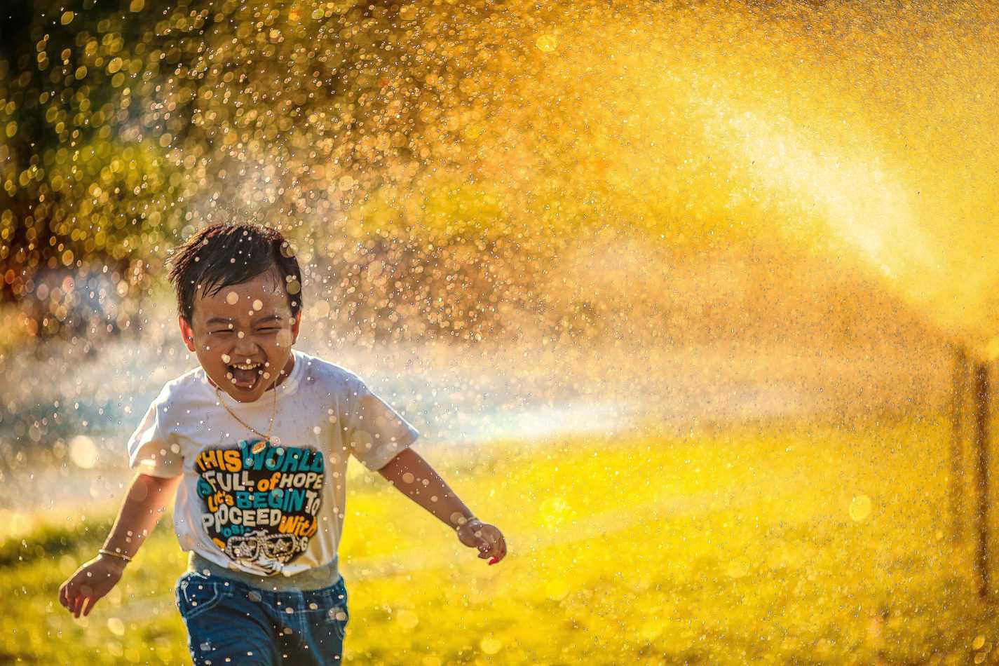 Boy running through water sprinkler