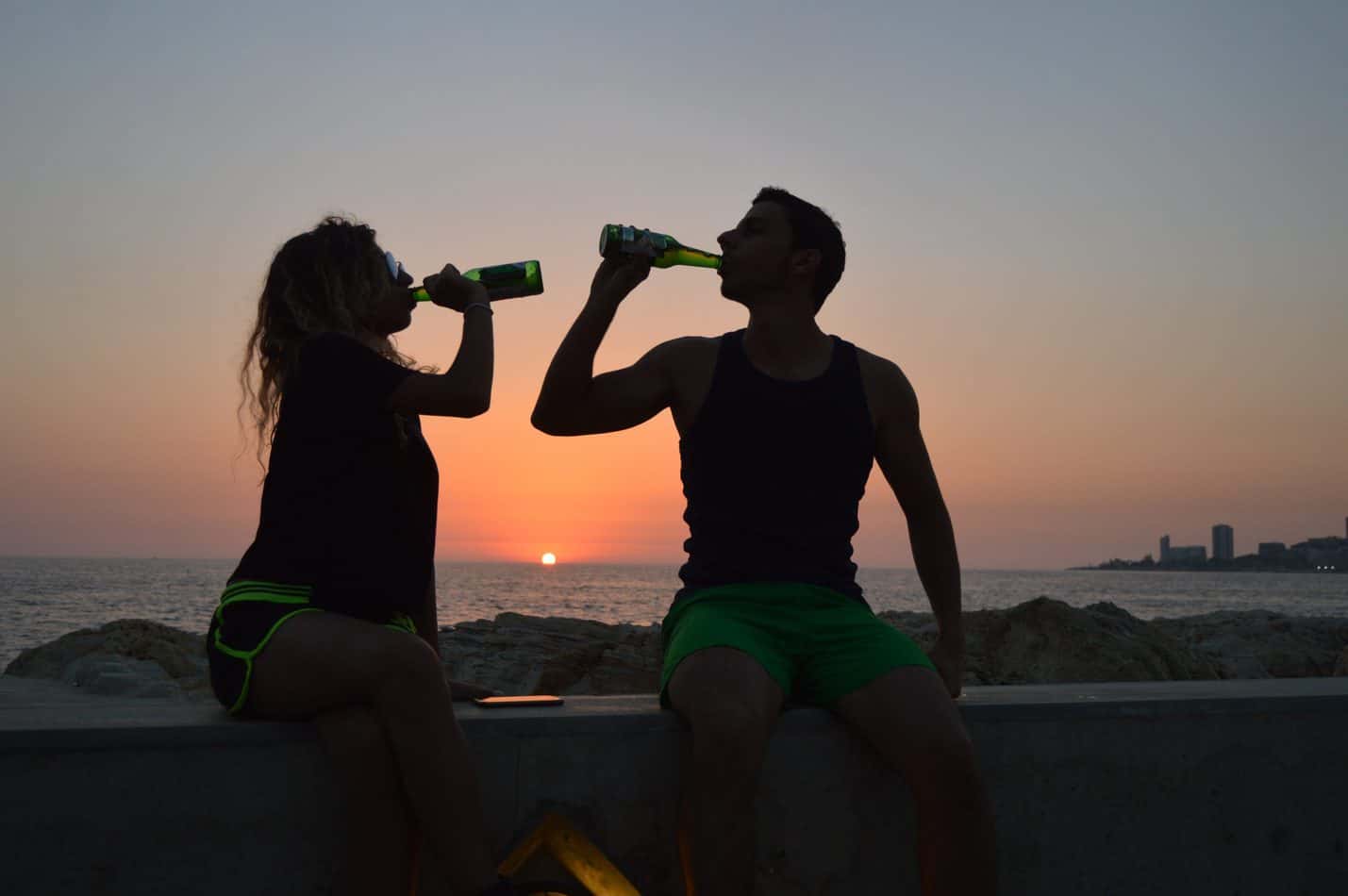 Two people drinking from bottles in the sunset.