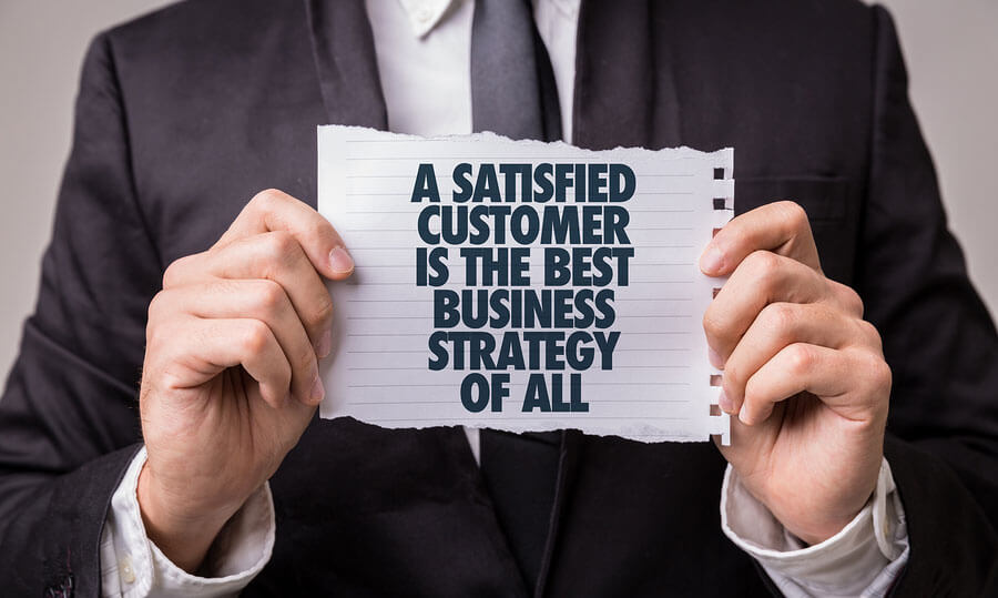 En man som håller upp en lapp där det står. A satisfied customer is the best business strategy of all.