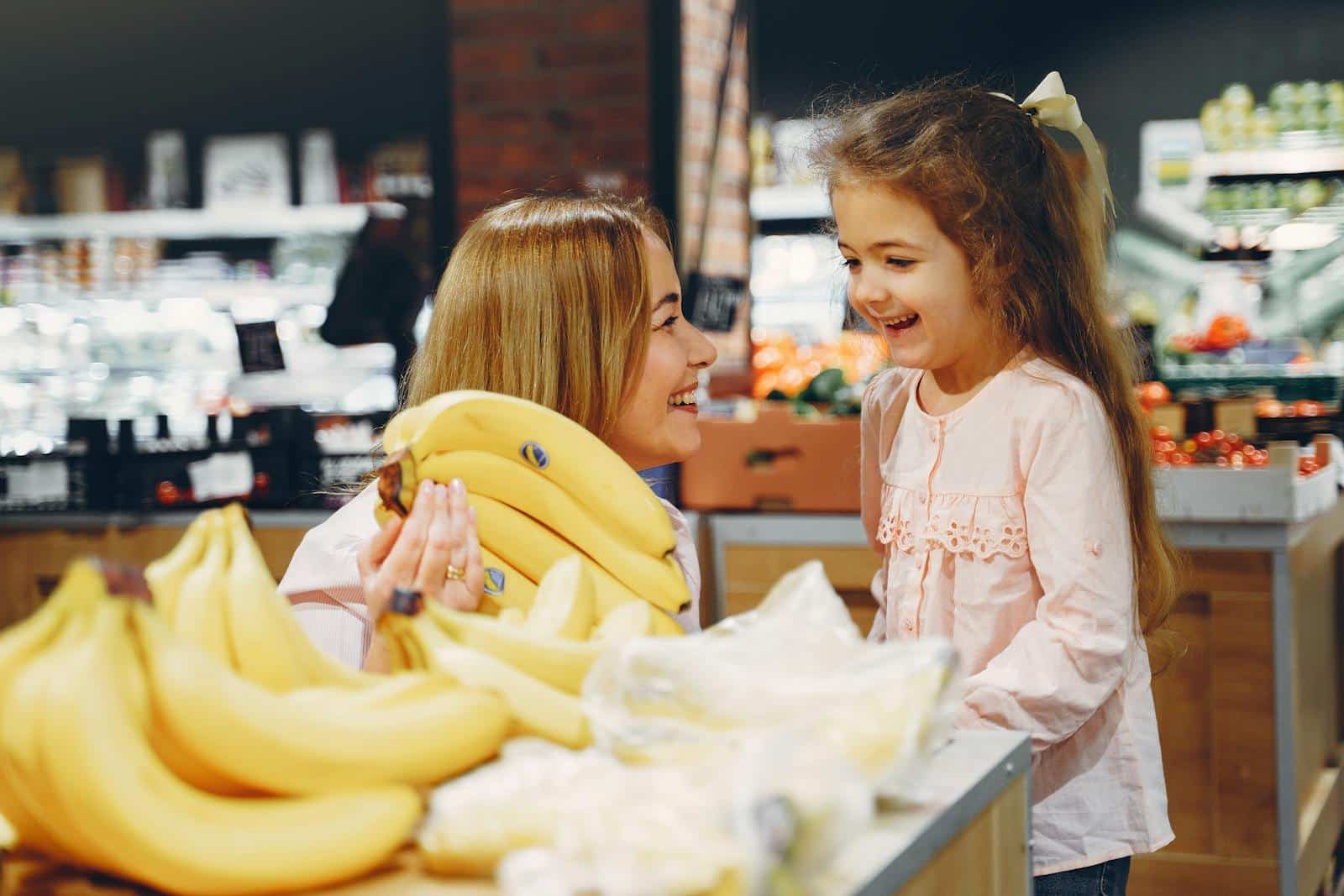 A joyful mother and daughter shopping for fresh bananas in a supermarket, sharing a happy moment.