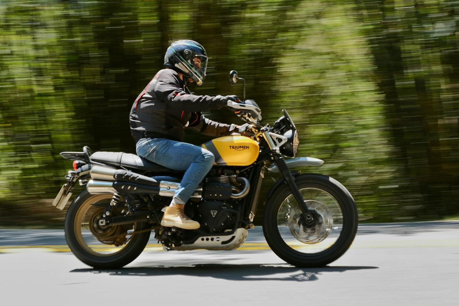 A biker riding a yellow Triumph motorcycle through a forest, capturing motion and speed.