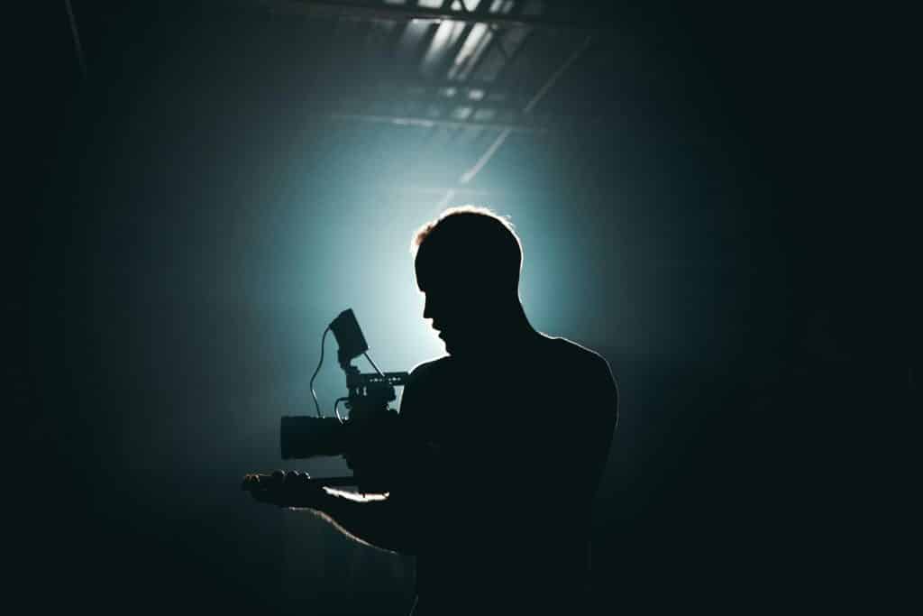 High contrast image with the outline of a man standing with a camera with bright light i front of him