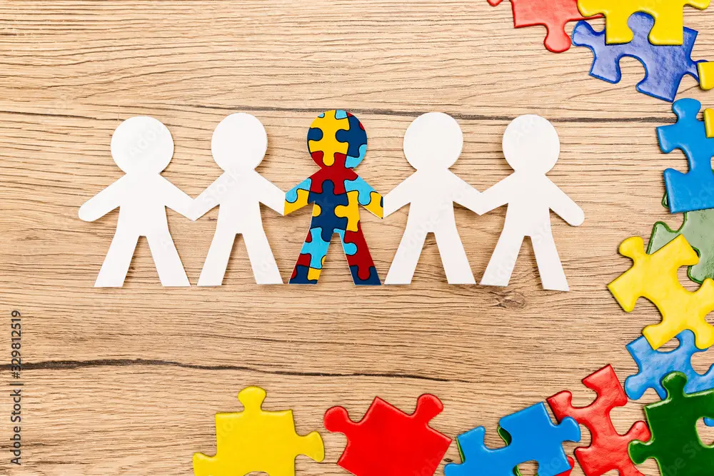 Paper cutout figures holding hands with one figure made of puzzle pieces on wooden background