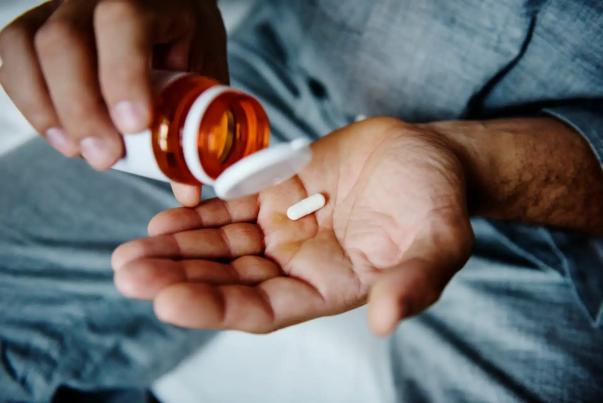 Person pouring capsule from prescription bottle into palm, medication management concept