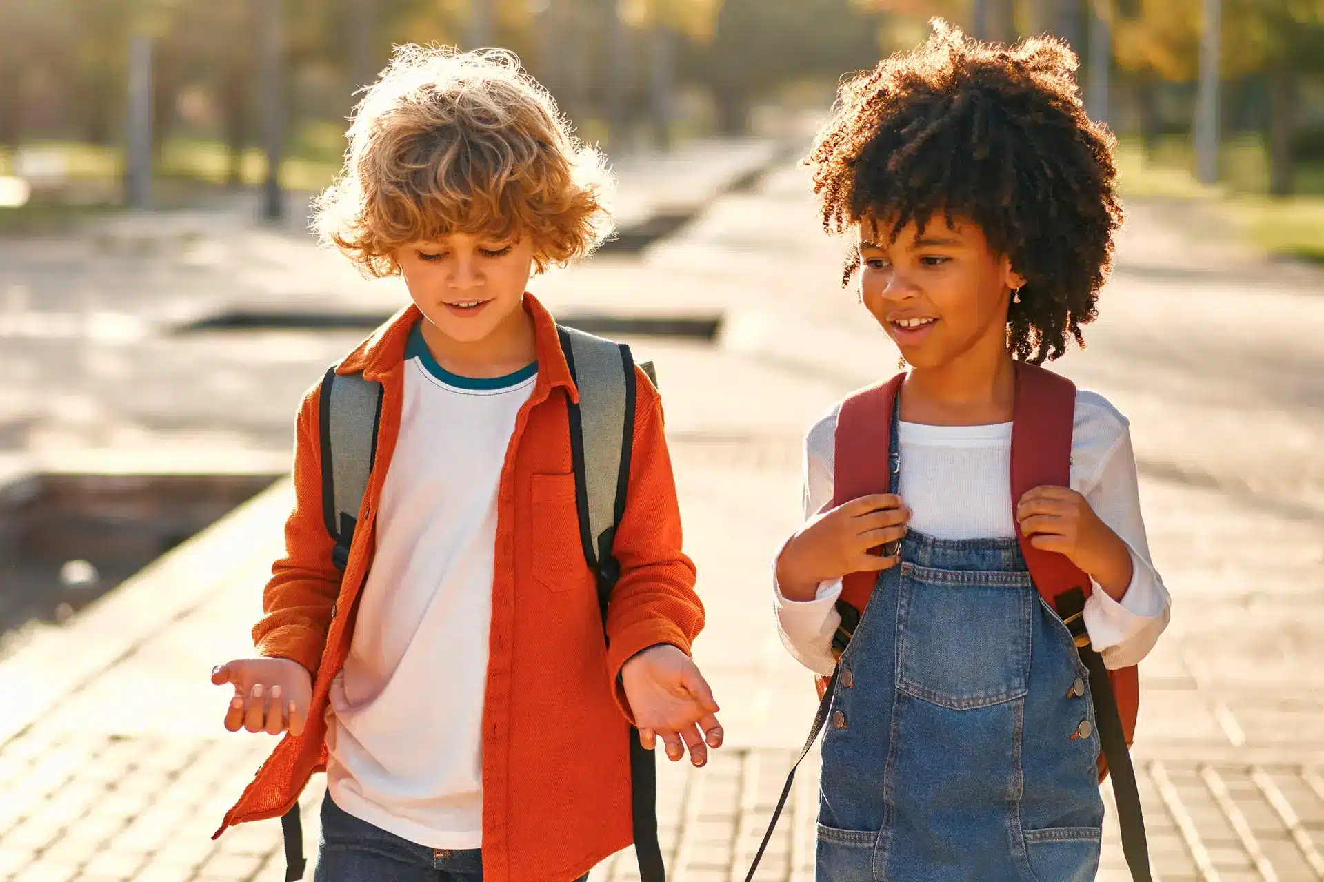 Two cheerful children walking with backpacks on a sunny day