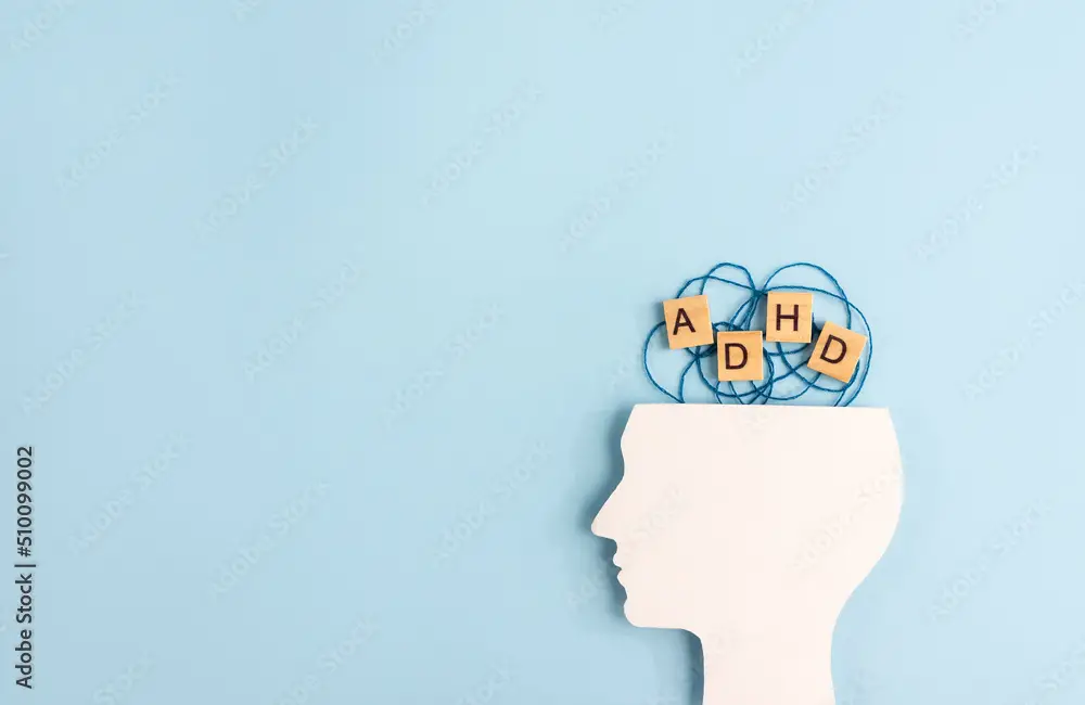 Silhouette of human head and wooden blocks with the letters ADHD on pastel background. Creative concept of attention deficit hyperactivity syndrome. Copy space