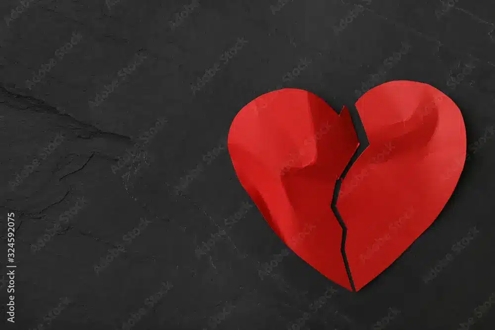 Red broken heart paper cutout on dark slate texture background