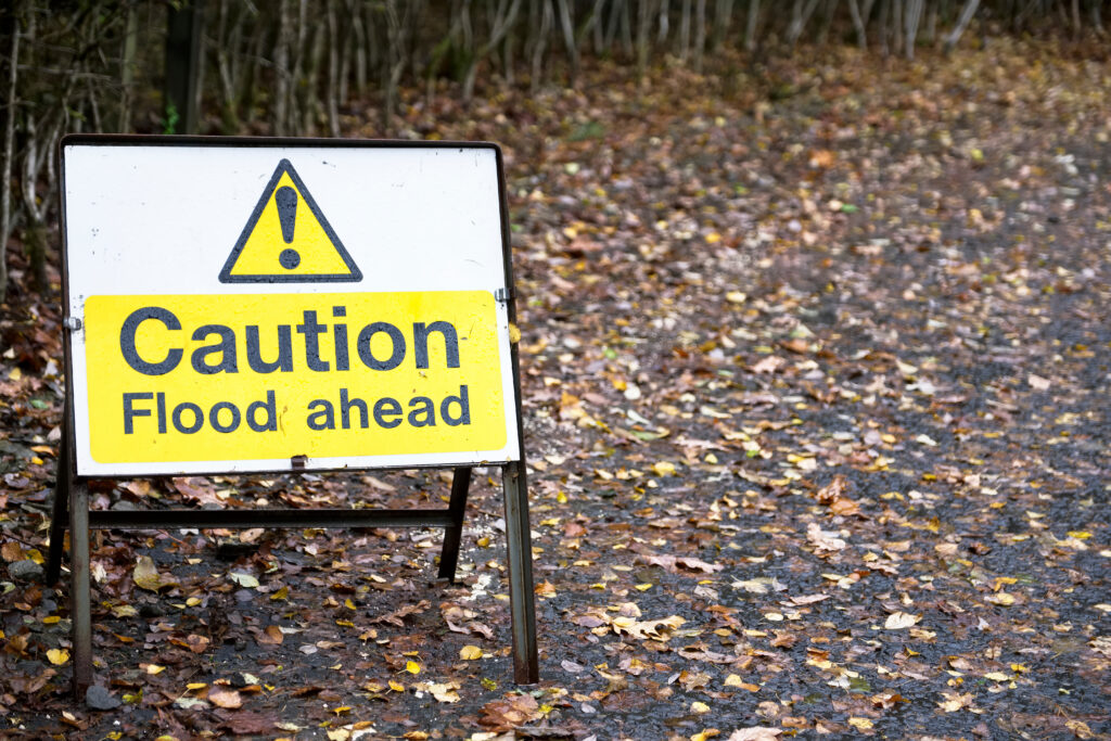 Caution flood ahead sign on Autumnal leafy road.