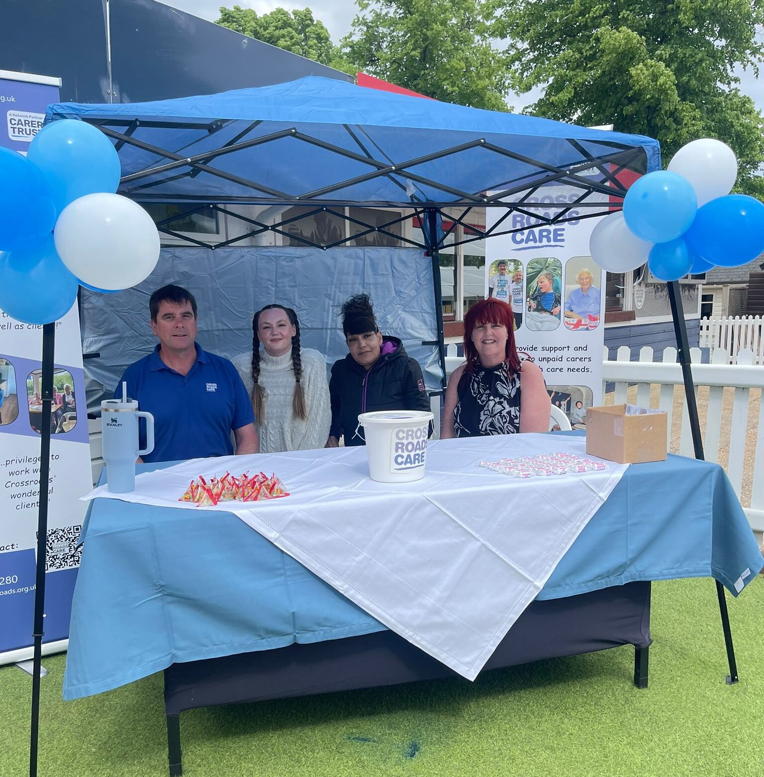 Four volunteers sitting under a blue pergola with balloons.