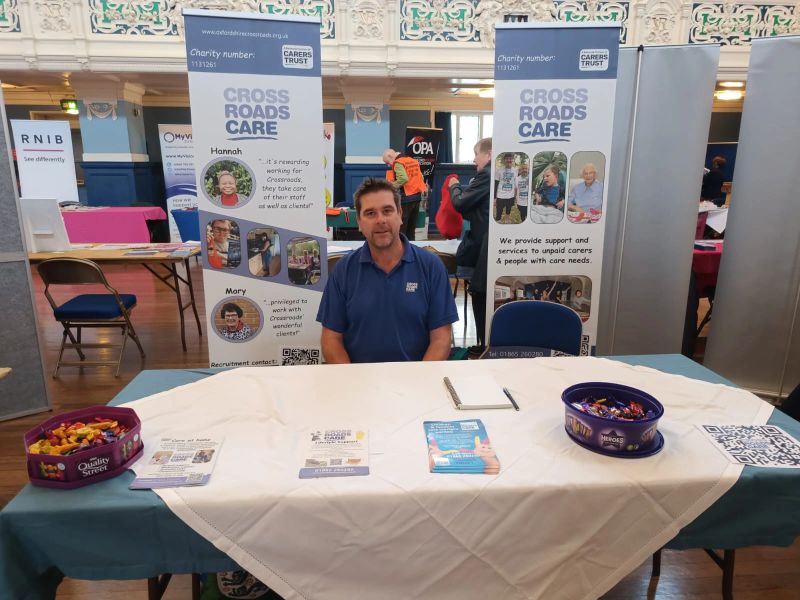 Care staff sat at table with chocolates with colourful banners behind.