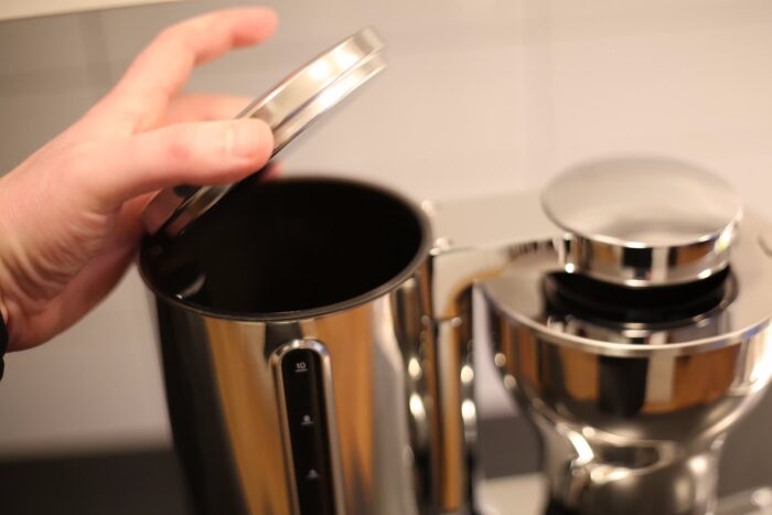En hand öppnar locket till vattentanken på Aarke Coffee Maker