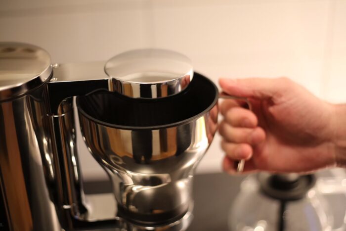 En hand håller i den avtagbara filterkorgen till Aarke Coffee Maker