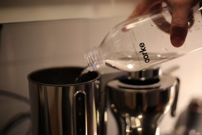 En hand häller vatten i vattentanken på Aarke Coffee Maker