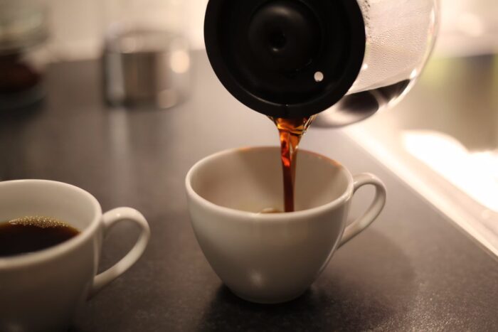 Kaffe hälls upp ur glaskannan från Aarke Coffee Maker i en keramikmugg