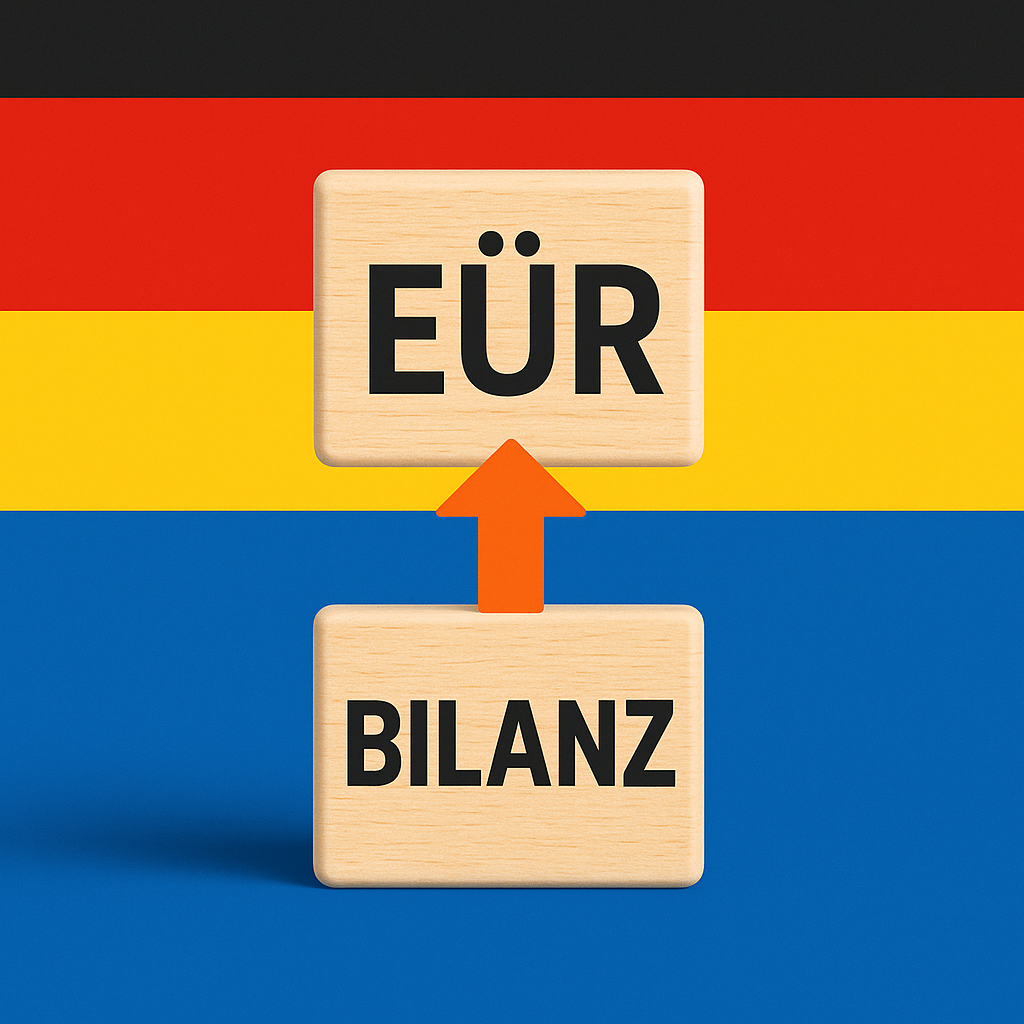 Dwa drewniane klocki z napisami „EÜR” i „Bilanz”, ustawione jeden na drugim, z pomarańczową strzałką skierowaną ku górze, na tle niemieckiej flagi i niebieskiego pasa.