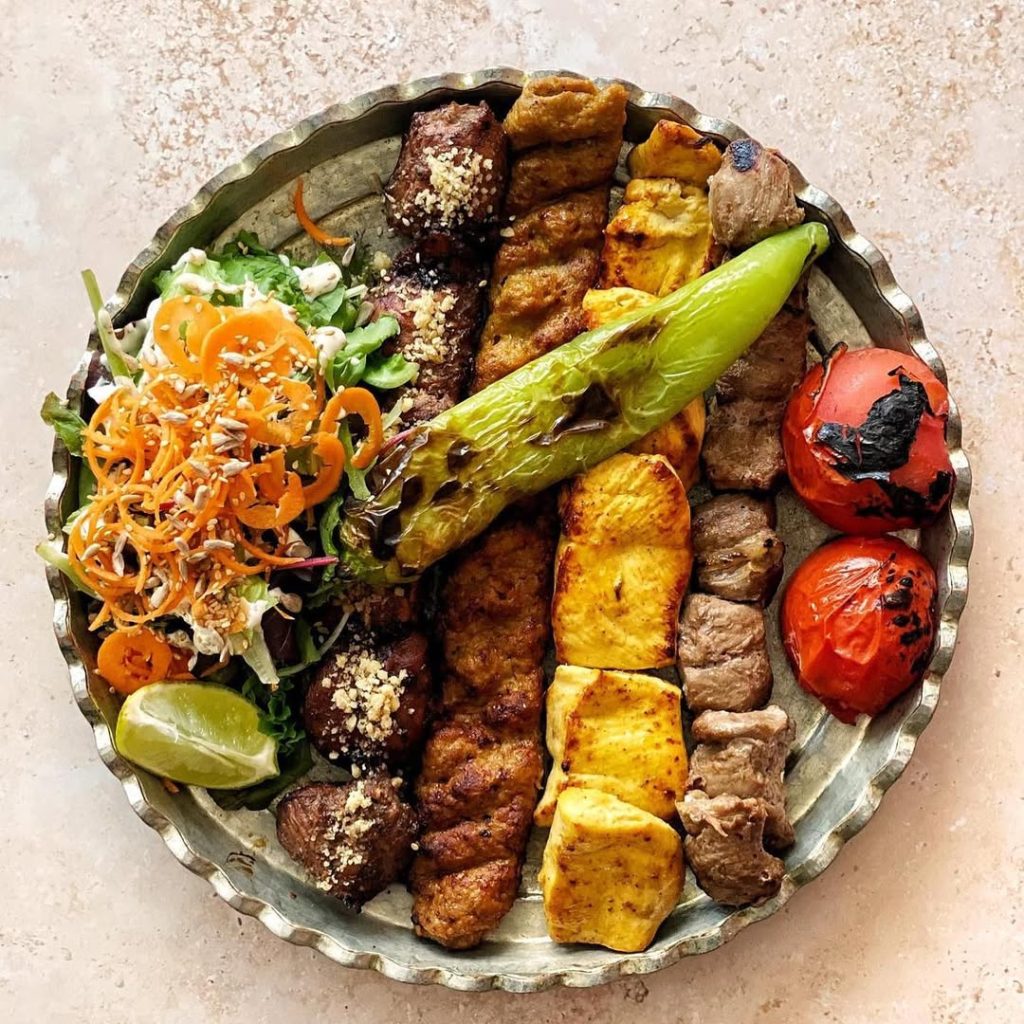 Grote feestelijke schotel met verschillende Perzische kebabs (zoals Kubideh, Jujeh), geserveerd met saffraanrijst, gegrilde tomaat en groenten in DARBAND restaurant te Kortrijk.