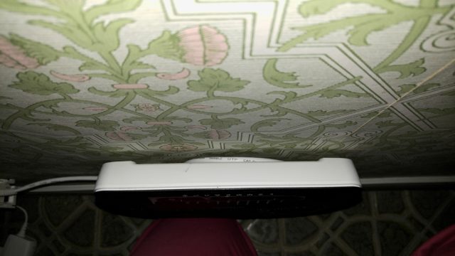 När man ser på Routern ovanifrån, framgår det att LAN-kabeln är "undangömd" bakom Routern och hänger över samma två skruvar som håller Routern på väggen. Installation av Telia Internet router och anslutning till fiberoptikdosan hos en kund på Djursholm.